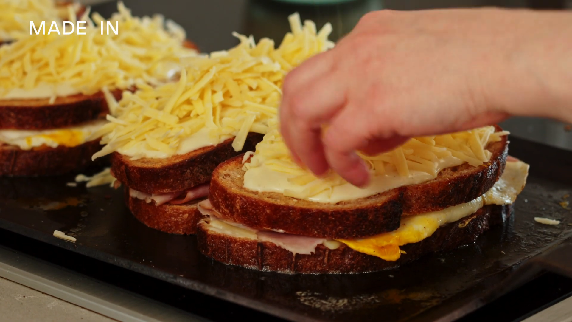 Grilled sandwich being topped with grated cheese
